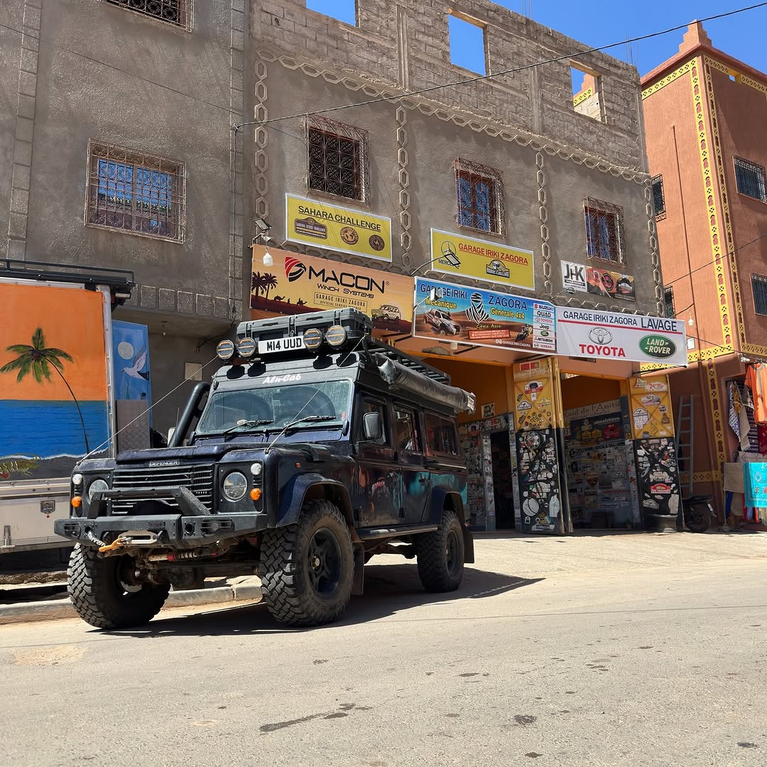 UK-registered Land Rover Defender 110 (M14 UUD) with Alu-Cab conversion parked in front of Garage Iriki in Zagora, Morocco