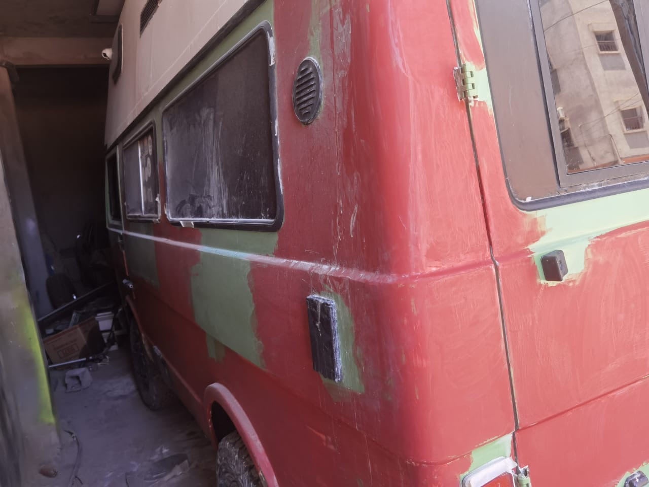 Close-up of the red and green rear side of the VW camper showing sanded areas prepped for filler and paint