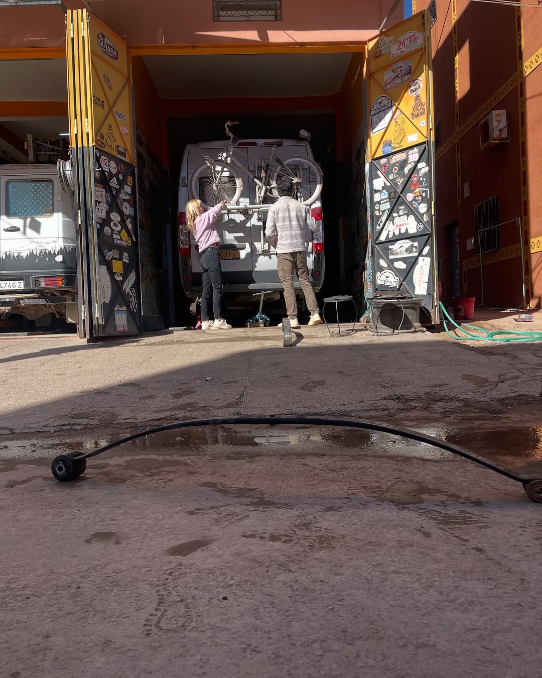 Reinforced leaf spring on the street in front of Garage Iriki while the owners inspect the rear of the Dutch Peugeot Boxer