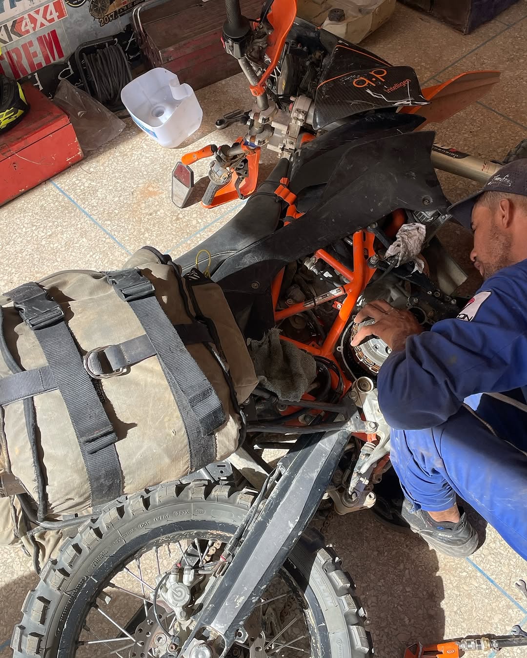 Garage Iriki mechanic replacing the clutch pack on an orange KTM enduro bike still loaded with desert luggage