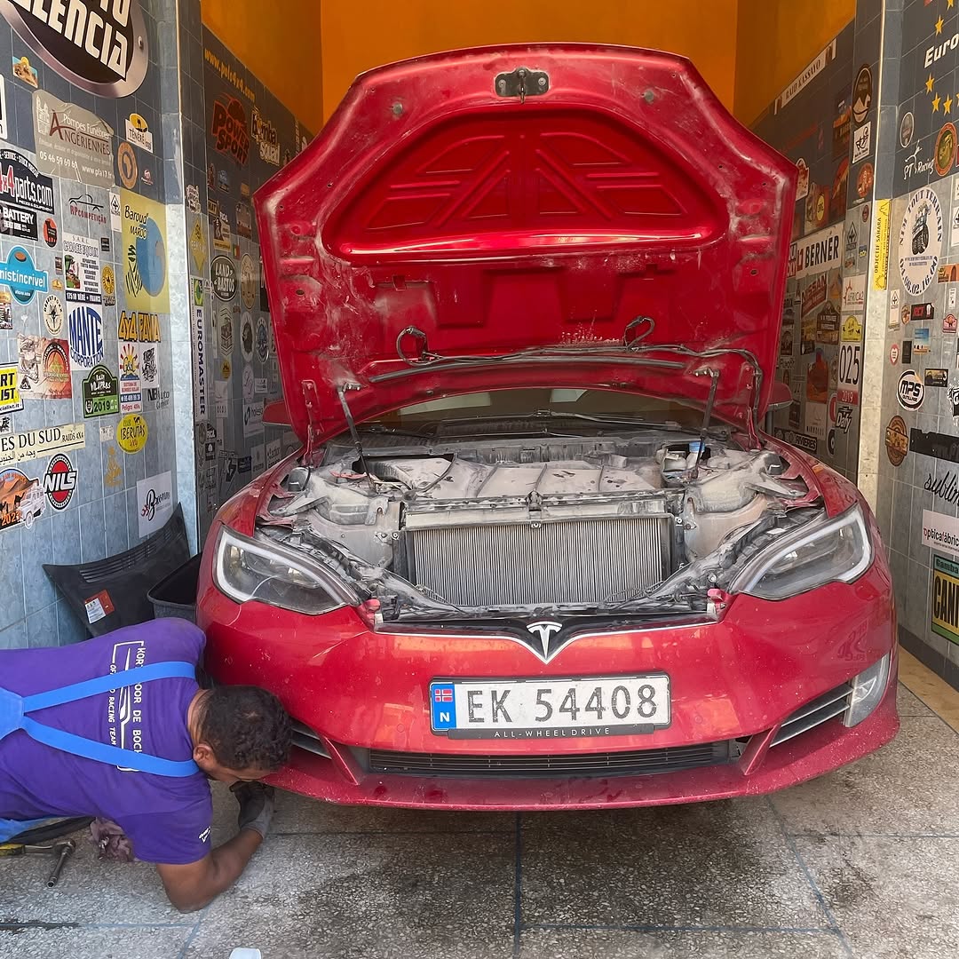 Front view of the red Tesla Model S with hood open while a Garage Iriki mechanic works on the front suspension lift