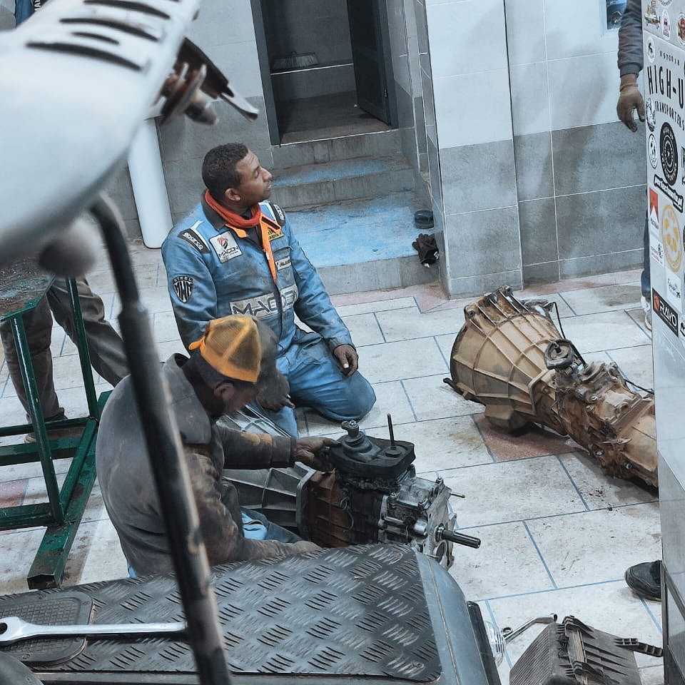 Two mechanics on the workshop floor working on the removed Land Rover Defender gearbox at Garage Iriki, Zagora