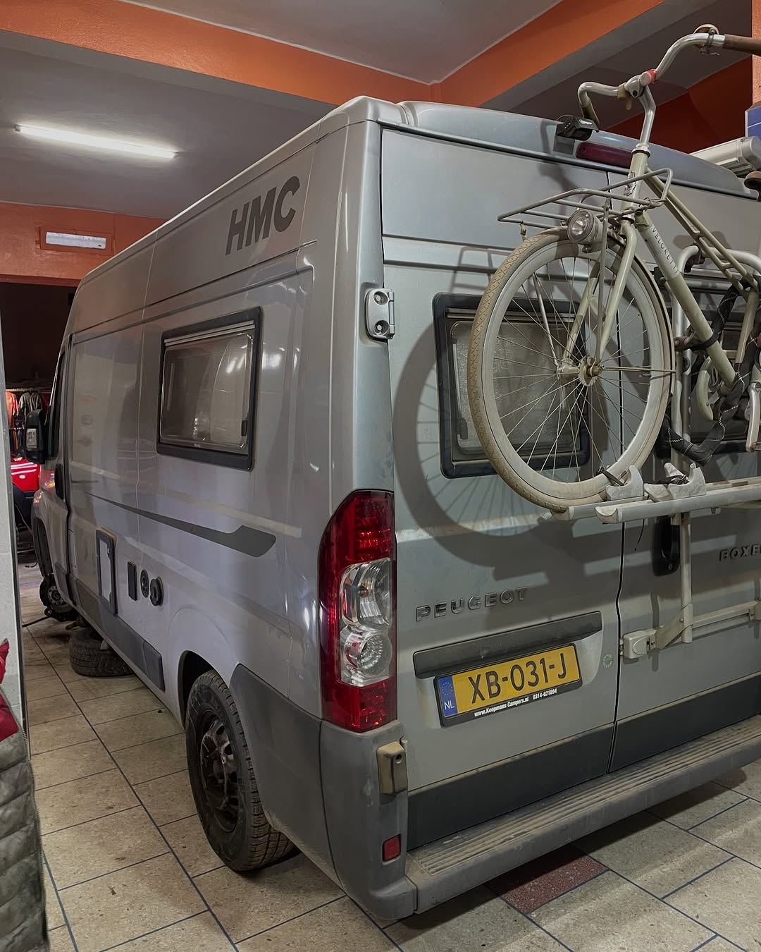 Rear view of the silver Peugeot Boxer HMC camper with mounted bicycle inside Garage Iriki after the rear suspension lift