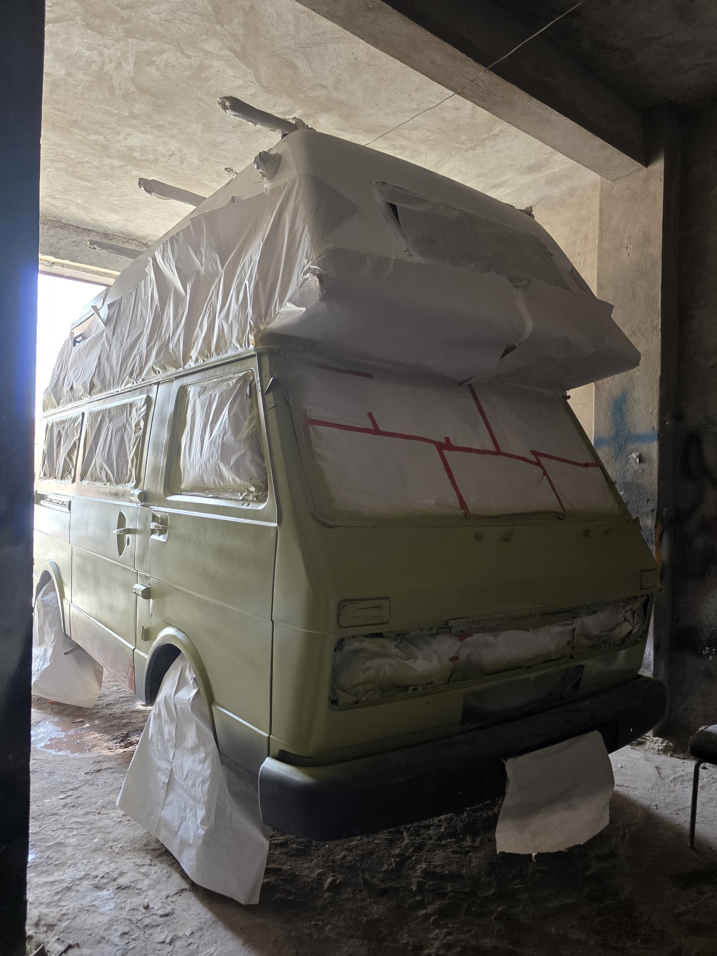 VW camper completely masked in paper and tape inside the paint booth, ready for the final coats