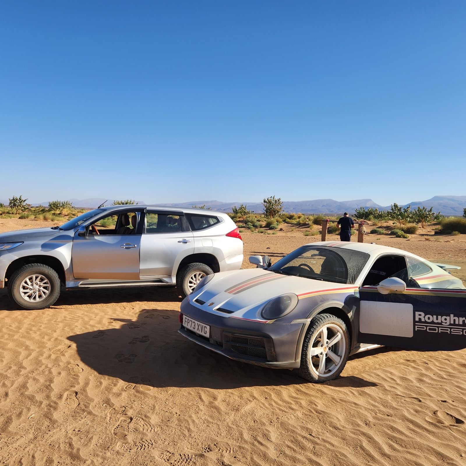 Porsche and Mitsubishi in sand between acacias