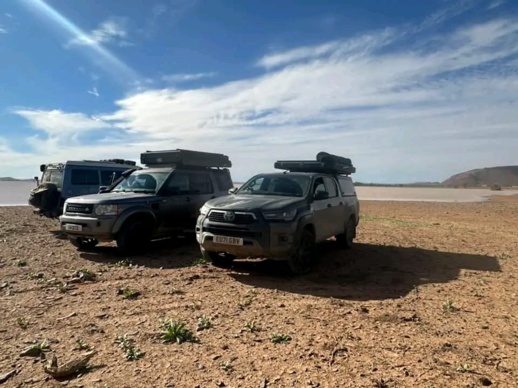 Overland vehicles stopped beside a wide open landscape
