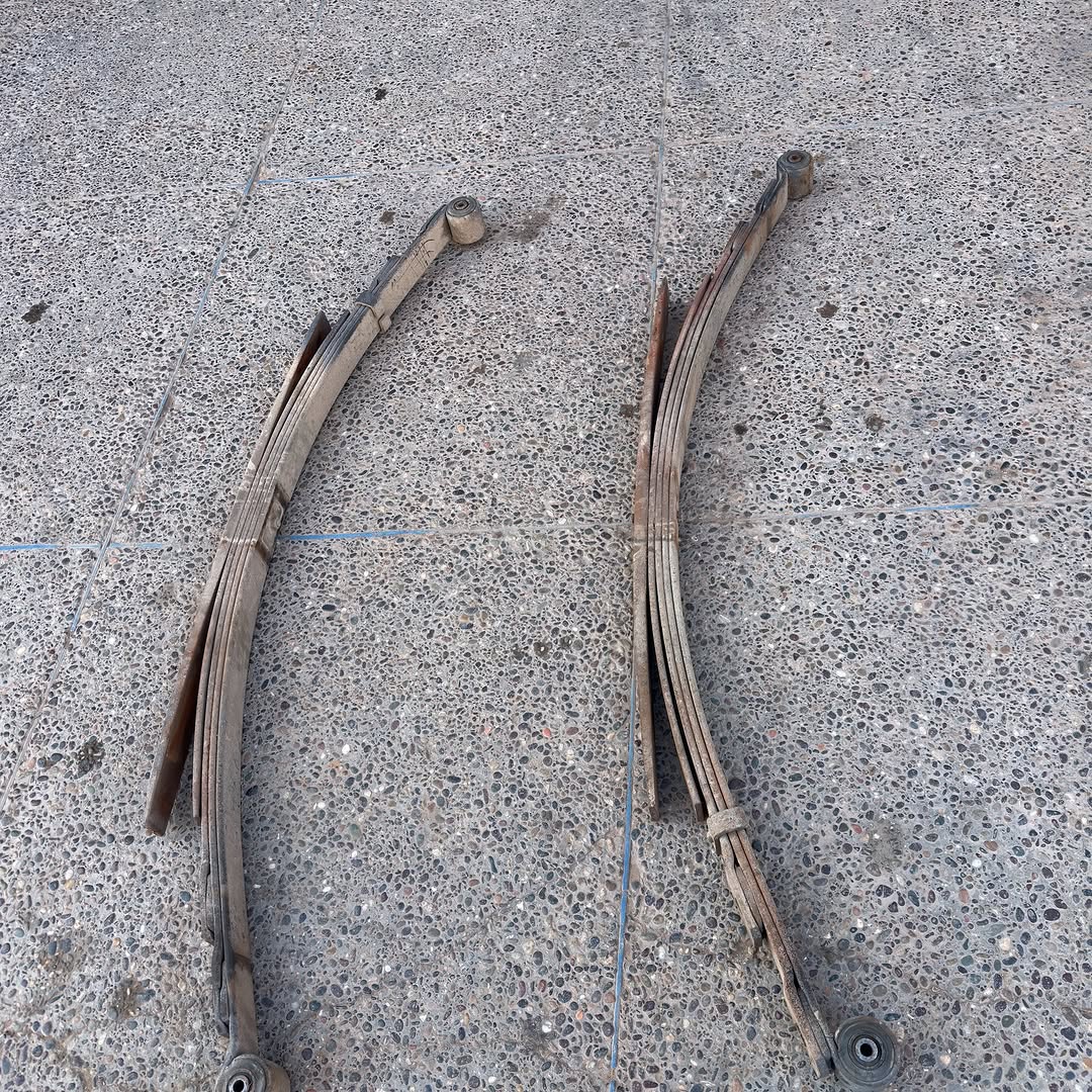 Two reinforced leaf spring packs laid out on the workshop floor before installation on the Mercedes 407D