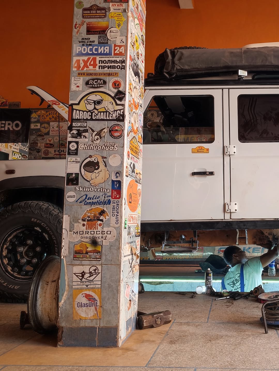 Overland sticker column at Garage Iriki next to the white Belgian Defender 110 during the rear suspension lift